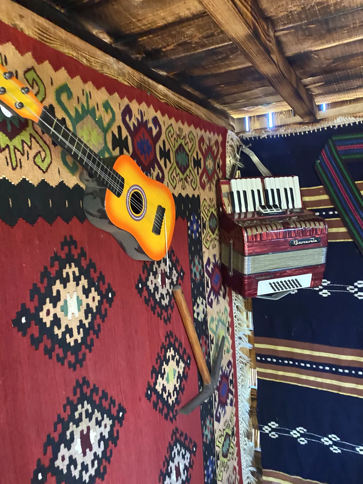 Crveni ćilim sa gitarom i malom harmonikom na zidu